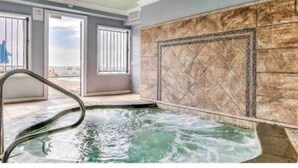 A spa area with a hot tub, a view of the sea through large windows, and a stone wall.
