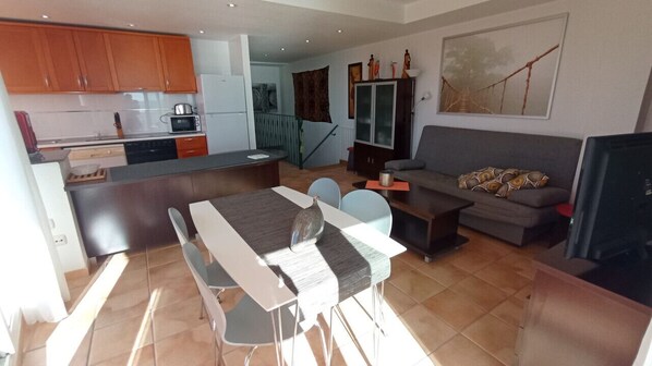 A modern kitchen with wooden cabinets, a dining area with a table and chairs, a gray sofa, and a television. - Apartamento Lidia 4 - Apartamento en residencia con piscina en Vinaròs - Ref. 287 (Vinaròs)