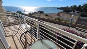Un balcón con vista al mar, una silla y una mesa.