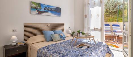 A bedroom with a bed, nightstand, and a view of the outdoors.