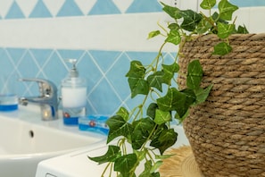 A bathroom with a white sink, a blue and white tiled wall, and a woven basket with green ivy. - Sardinia Re - Il Poggio 6 (Badesi)