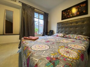 Una camera da letto con un letto grande, una testiera, una finestra con tende, uno specchio e un quadro appeso al muro.