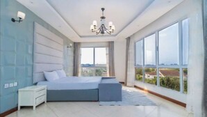 Een moderne slaapkamer met een groot bed, een nachtkastje, een kroonluchter en uitzicht op de stad door grote ramen.