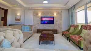 Een woonkamer met een flatscreen televisie aan een stenen muur, een plafondventilator en twee banken met bloemenmotief.