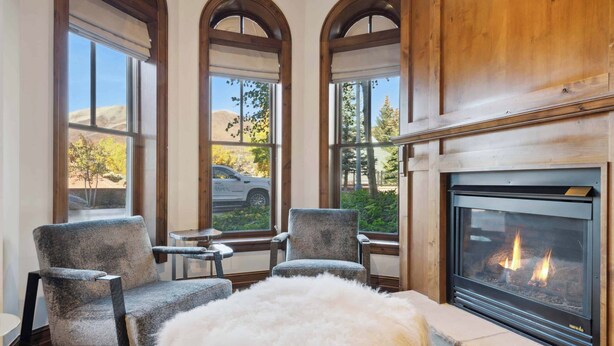 A cozy room with a fireplace, two armchairs, a white fur throw, and large windows offering a view of the outdoors. - The Aspen Mountain Residences 02A - Studio Residence (Aspen)