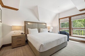 Ein Schlafzimmer mit einem großen Bett, einem Nachttisch mit Lampe, einem Sessel und einem Fenster mit Blick auf Grünflächen.