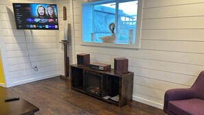 A living room with a flat-screen TV mounted on the wall, a fireplace with a decorative swan, a wooden entertainment unit with speakers, and a purple armchair. - Beautiful mountain views, Close to trails, Pet friendly Farm Awaits you! (Florence)