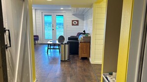 A hallway with wooden flooring leading to a dining area with a table and chairs, a trash can, and a view through a door. - Beautiful mountain views, Close to trails, Pet friendly Farm Awaits you! (Florence)