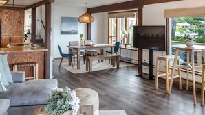 A spacious living area with a high ceiling, wooden beams, a central chandelier, and a large window offering a view of the outdoors. - Beachfront House Getaway with Amazing Views&Access (Port Orchard)