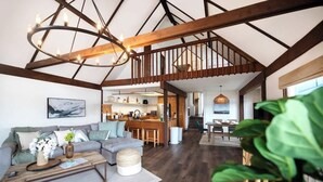 A spacious loft with a high ceiling, exposed wooden beams, a central staircase, a kitchen area, and a living room with a sofa and coffee table. - Beachfront House Getaway with Amazing Views&Access (Port Orchard)