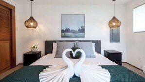 A hotel room with a bed, two bedside tables, a nightstand, a green throw blanket, a heart-shaped towel arrangement, a painting on the wall, and two hanging lamps. - Beachfront House Getaway with Amazing Views&Access (Port Orchard)