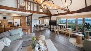A spacious living area with a wooden staircase, a dining set, and a large window overlooking a scenic view. - Beachfront House Getaway with Amazing Views&Access (Port Orchard)
