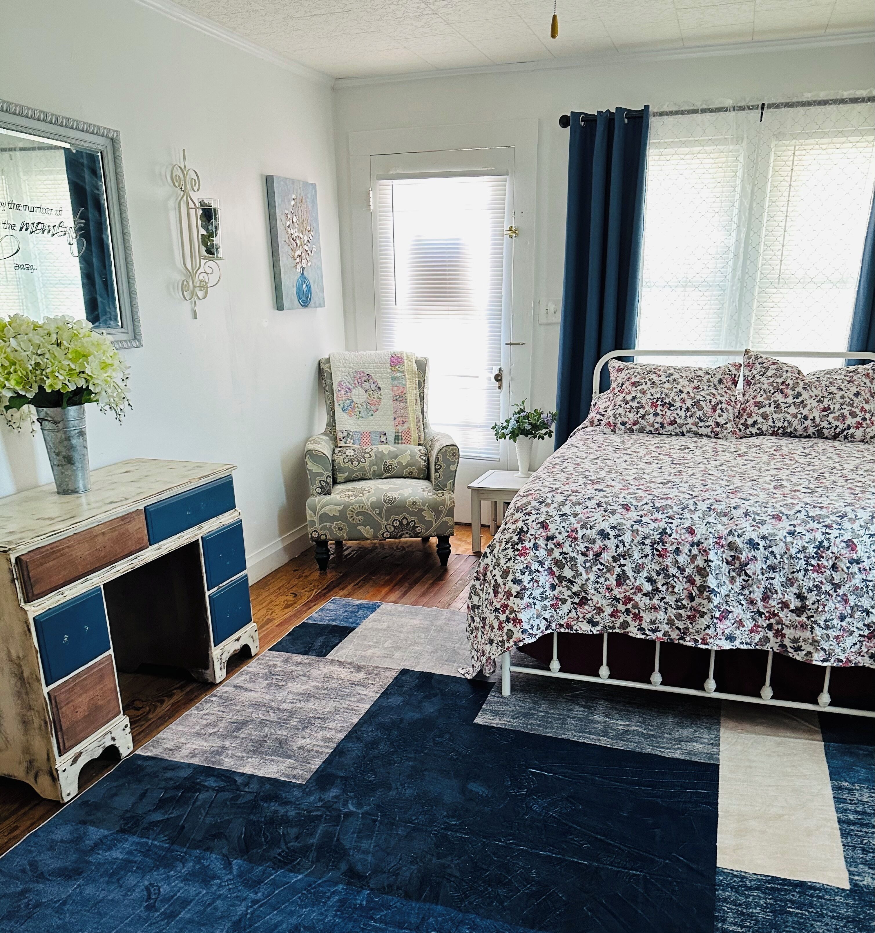 Une chambre à coucher avec un lit, une chaise, une commode et une fenêtre avec des rideaux.