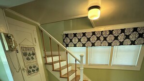 Eine Treppe mit Holzbodenstufen und weißen Geländern, eine Tür mit Telefon und ein Fenster mit Jalousien.