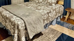 Ein ordentlich eingerichtetes Schlafzimmer mit einem Bett, einem Nachttisch, einer Lampe, einem Gemälde und einem kleinen Tisch.