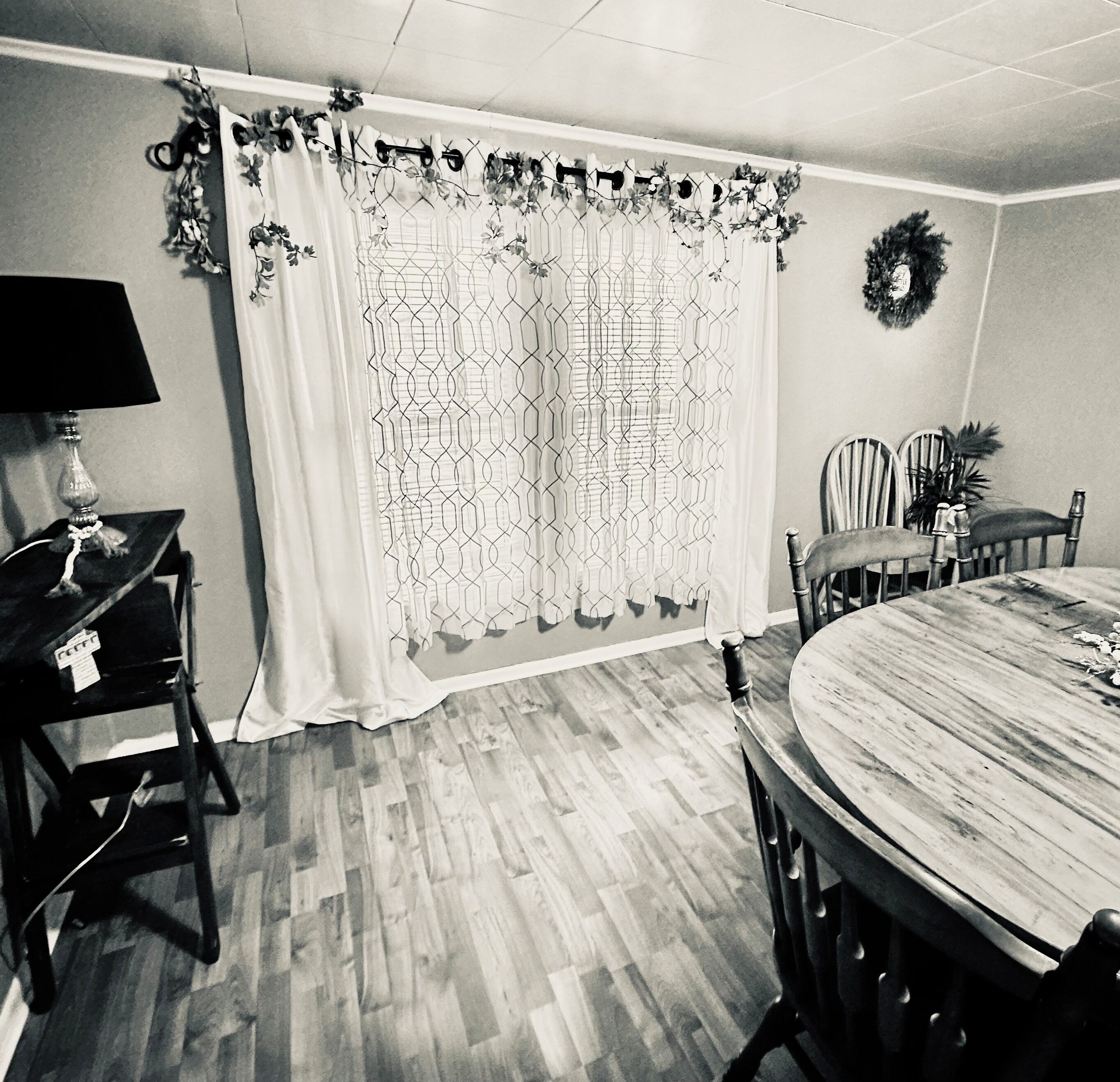 A dining area with a round wooden table, two chairs, a black lamp, and a decorative curtain with floral patterns.
