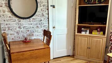 Una habitación con una mesa de comedor de madera, sillas, un tapete estampado, un espejo, una puerta blanca y un mueble de madera con un televisor.