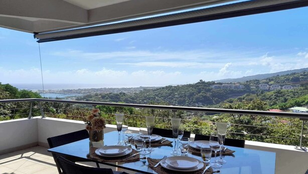 A dining table set for four on a balcony with a clear view of a coastal landscape. - TAHITI OCEAN VIEW HOME (Papeete)