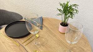 Una mesa redonda de madera dispuesta con platos negros, cubiertos dorados y dos copas de vino.