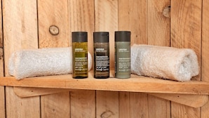 A wooden shelf with three bottles of Anyah Eco Spa Treatment and a rolled white towel. - Ashdown Luxury Dome (Hoath)