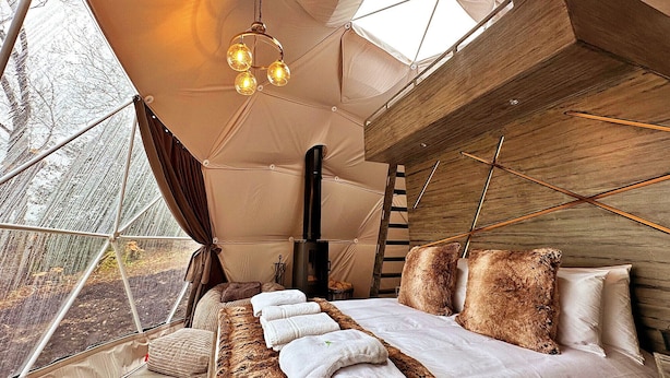 A cozy bedroom with a large bed, a hanging light fixture, and a view through a window. - Ashdown Luxury Dome (Hoath)