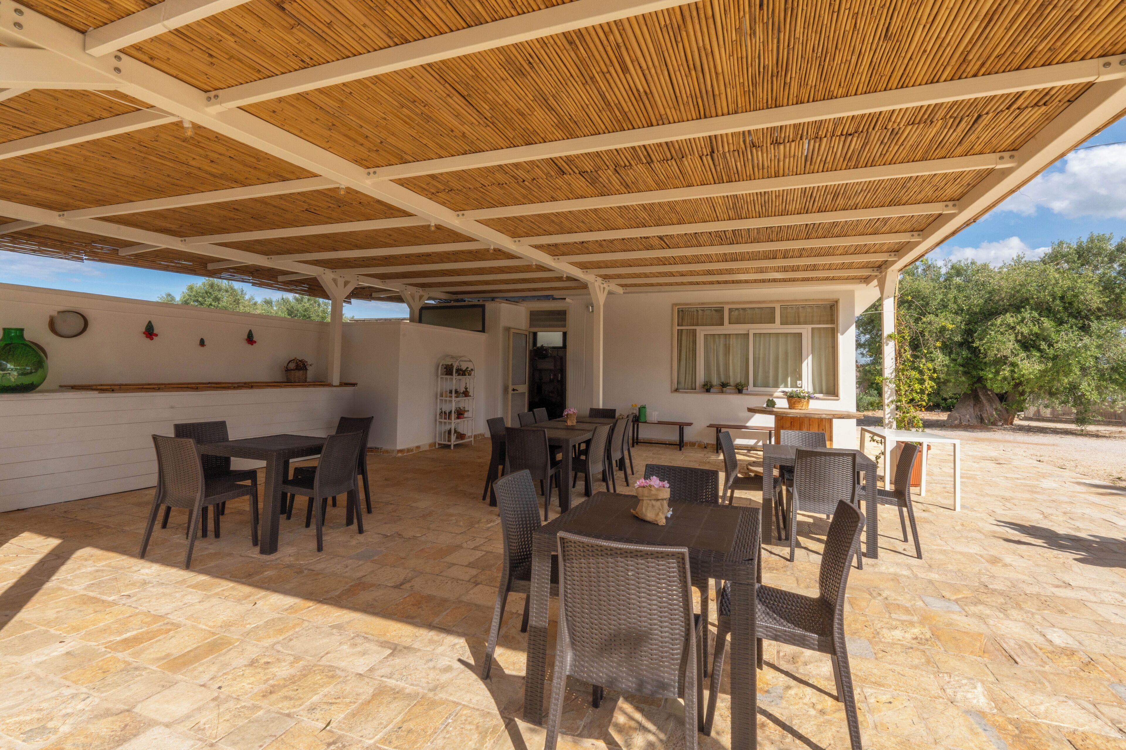 Patio esterno con tetto in legno, pavimento in pietra e mobili in vimini.