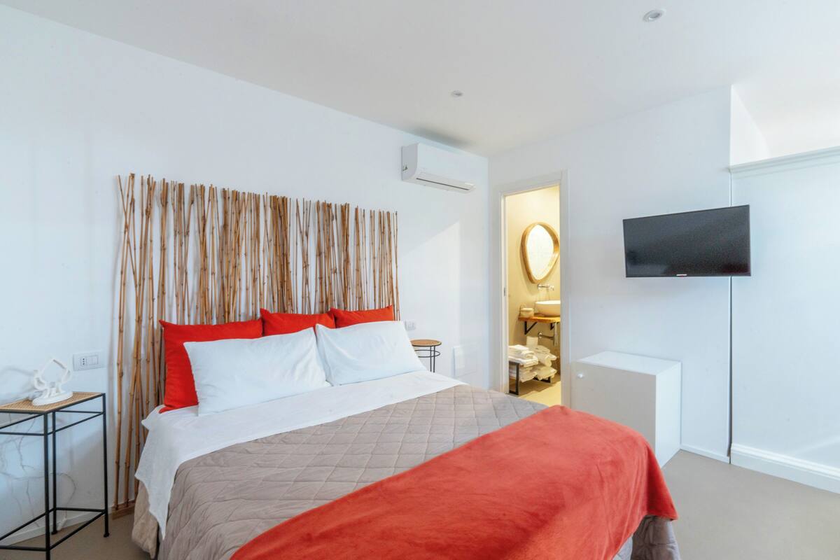 Habitación de hotel con cama, televisor montado en la pared y baño visible a través de una puerta abierta.