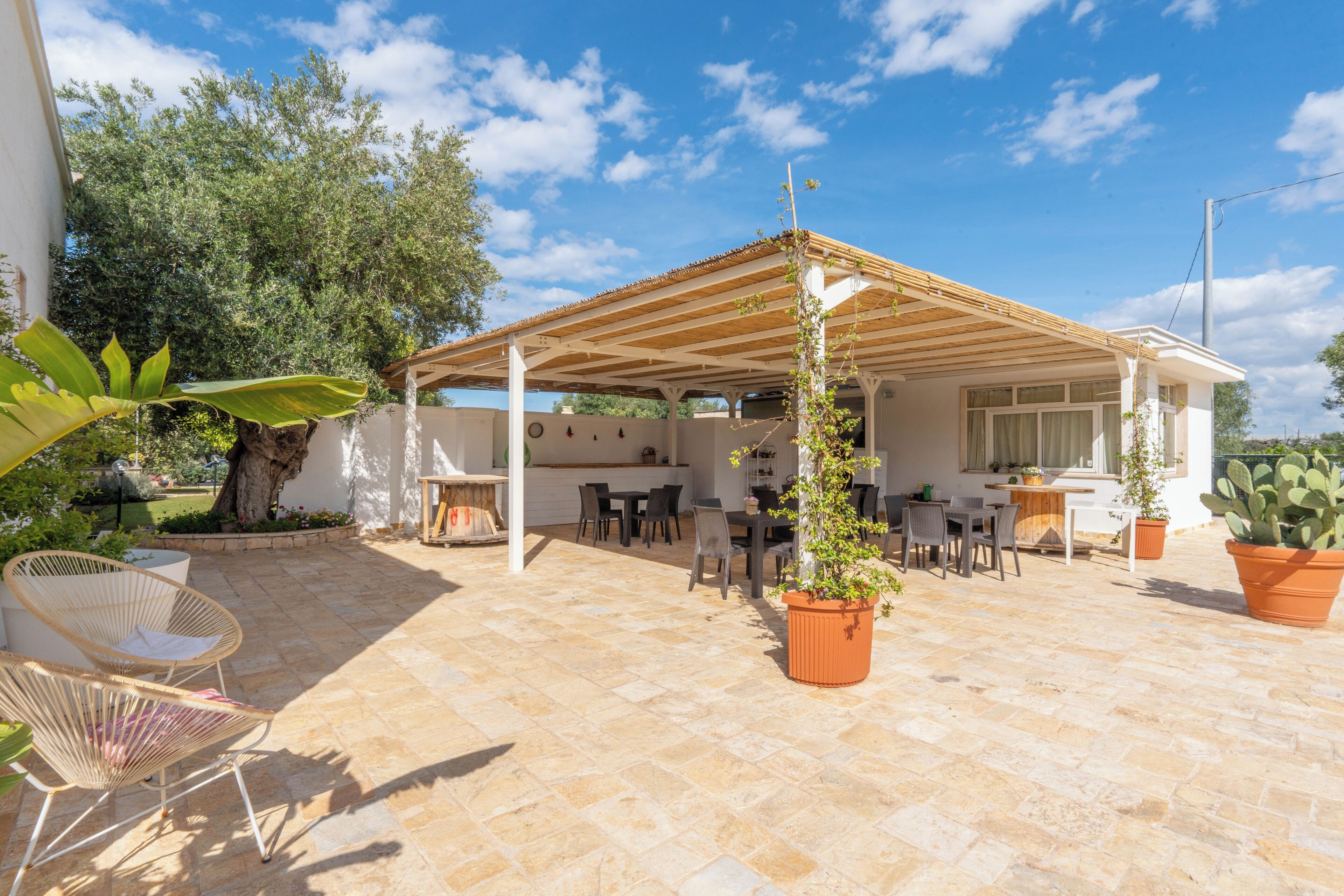 A covered outdoor patio with stone flooring, wooden furniture, and potted plants.