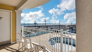 Un balcon avec des chaises blanches, une piscine et une vue sur la plage et l’océan.