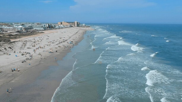 Une plage avec une longue étendue de sable, quelques personnes et des bâtiments en arrière-plan.