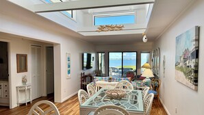 A dining area with a glass-top table, white chairs, and a view of the sea through large windows. - WATERFRONT!!!  Literally on the water of beautiful Bogue Sound. No better view. (Atlantic Beach)