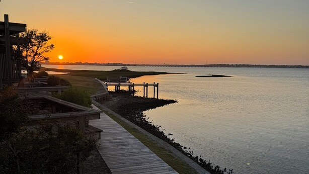 A wooden boardwalk leading to a dock by a calm body of water during sunset. - WATERFRONT!!!  Literally on the water of beautiful Bogue Sound. No better view. (Atlantic Beach)