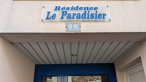 Rakennuksen sisäänkäynti, jossa on kyltti, jossa lukee ”Résidence Le Paradisier”, ja numerokilpi, jossa on numero ”9 BIS”.
