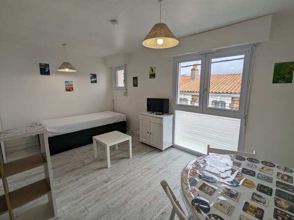 A small, well-lit room with a bed, a desk, a TV, and a window with a view of buildings.