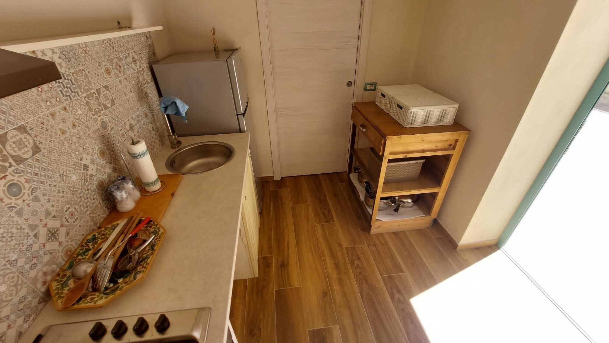 A compact kitchen with a sink, a wooden shelf unit, and a patterned backsplash.