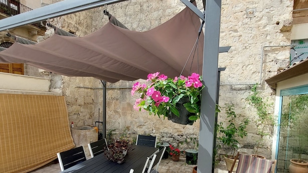 Un patio al aire libre con una mesa y sillas, una maceta colgante y plantas en macetas.