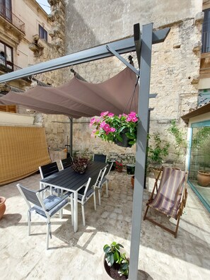 An outdoor patio with a table and chairs, a hanging flower pot, and potted plants. - Casa Conti. Elegante Pied à Terre nel Centro Storico di Scicli Perla del Barocco (Scicli)