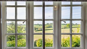 A large window with multiple panes, offering a view of a green landscape with fields and trees. - 3 Bed in Tavistock (oc-t29334) (Gulworthy)