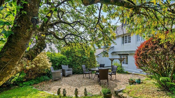 A garden with a patio area featuring wicker furniture and a white building in the background. - 3 Bed in Tavistock (oc-t29334) (Gulworthy)