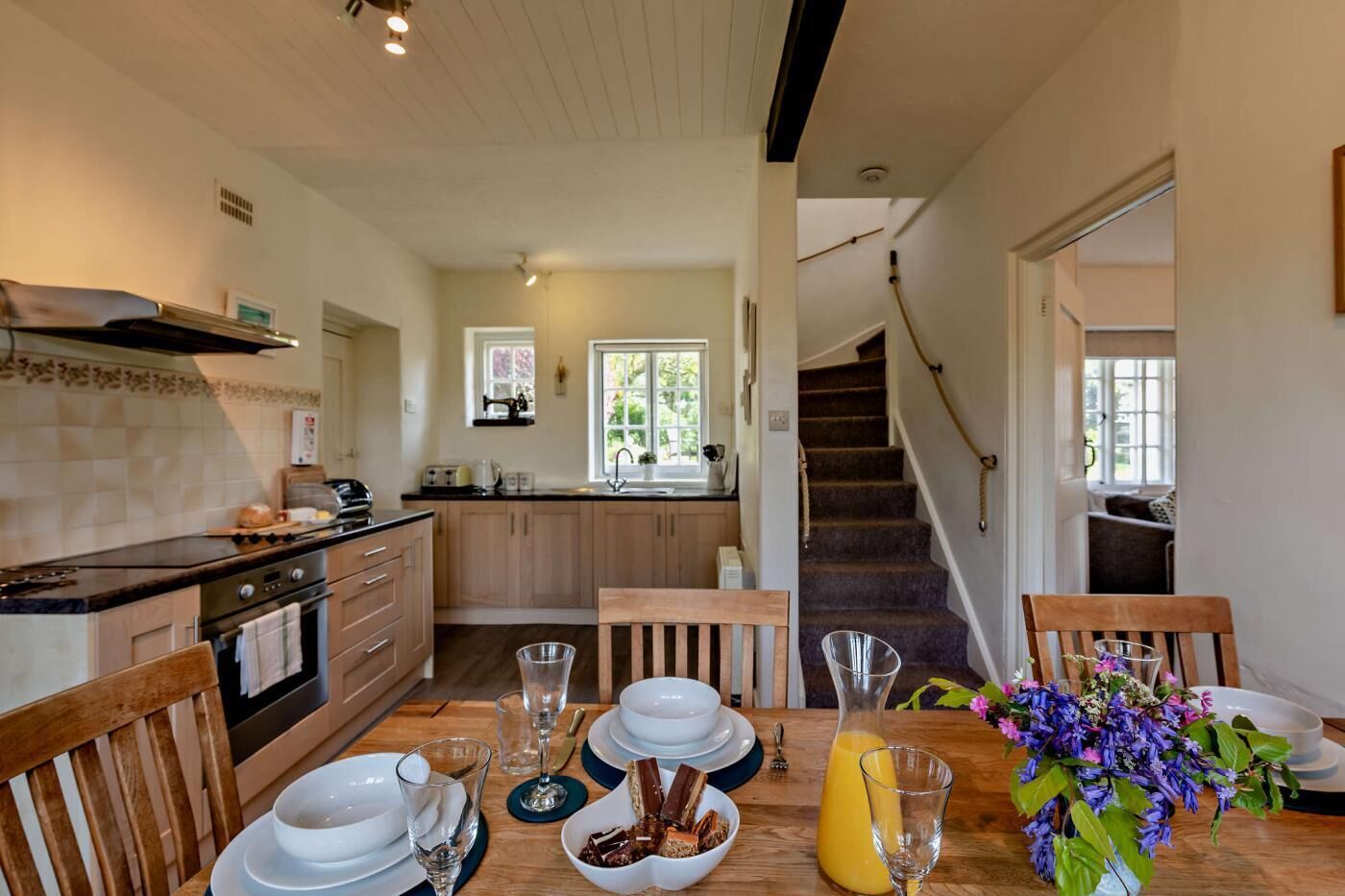 Une cuisine moderne avec des meubles en bois, un four encastré et un coin repas doté d’une table en bois, mise pour le petit-déjeuner.