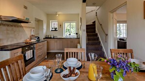 A modern kitchen with wooden cabinets, a built-in oven, and a dining area with a wooden table set for breakfast. - 3 Bed in Tavistock (oc-t29334) (Gulworthy)