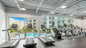 Ein Fitnessraum mit Laufbändern, Crosstrainern und Blick auf einen Pool und Gebäude.