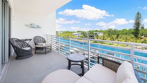 Ein Balkon mit Korbmöbeln, einem kleinen Tisch und Blick auf einen Swimmingpool und Grünflächen.