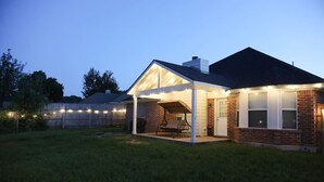 A house with a covered patio, a brick exterior, and a fenced backyard. - Spacious TX Oasis – Game Room, PS5, Xbox, & BBQ (Fort Worth)