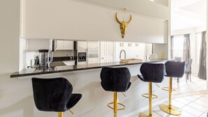 A modern kitchen with a bar area, stainless steel appliances, and a bull's head decoration. - Spacious TX Oasis – Game Room, PS5, Xbox, & BBQ (Fort Worth)