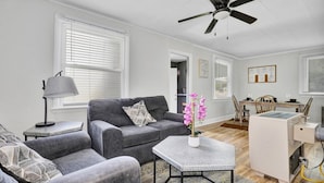 A modern living room with a grey sofa, a coffee table, a ceiling fan, and a dining area with a table and chairs. - Quaint 1 Bedroom House on N Martin Luther King Jr Blvd, Lansing: Your Ideal Home (Lansing)