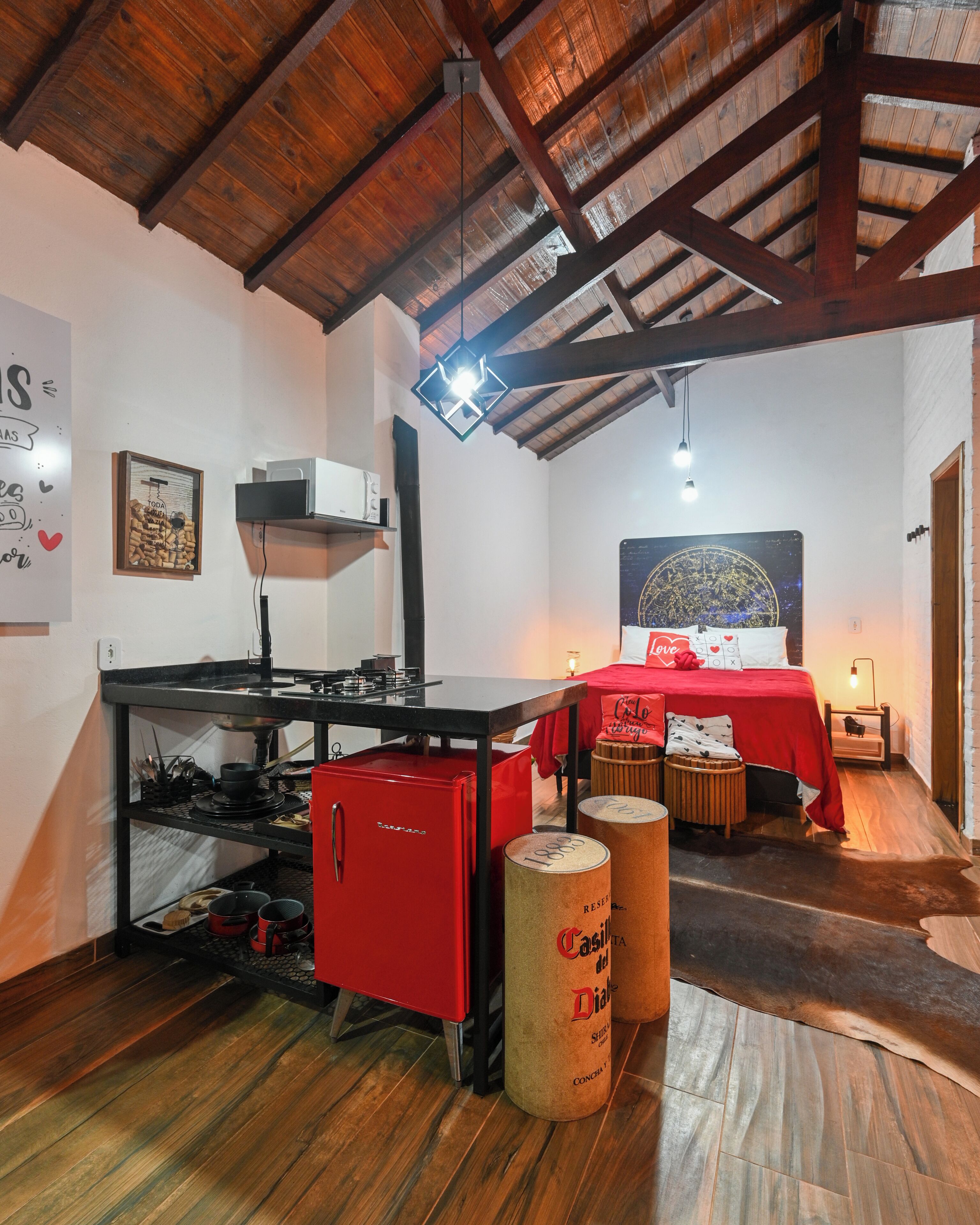 Een rustieke kamer met een houten plafond, een bed met een rode sprei, een klein tafeltje en een rode apparate.