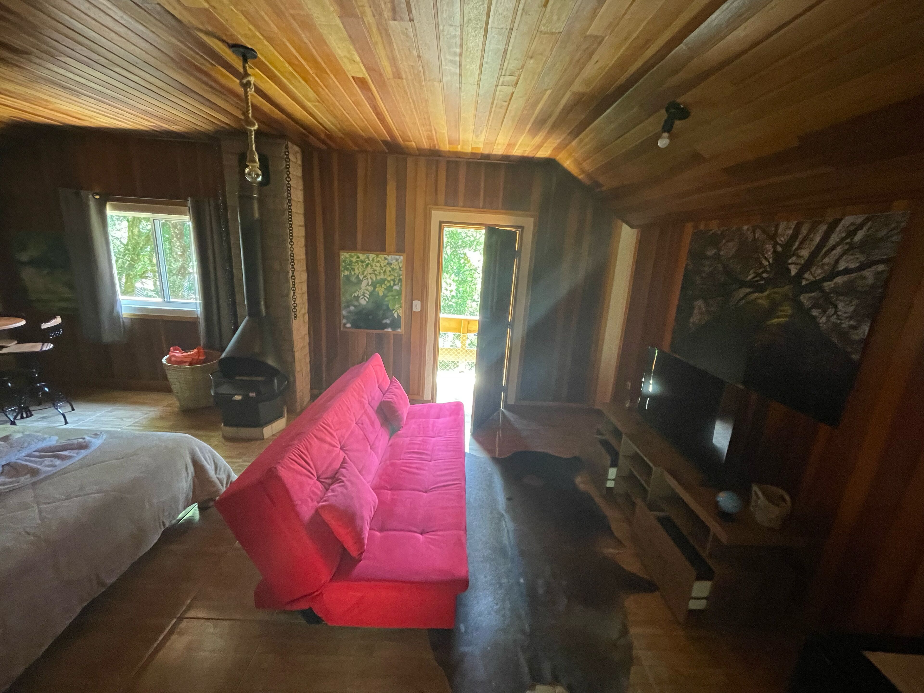 A cozy cabin interior with a red sofa, wooden walls, a fireplace, and a television.