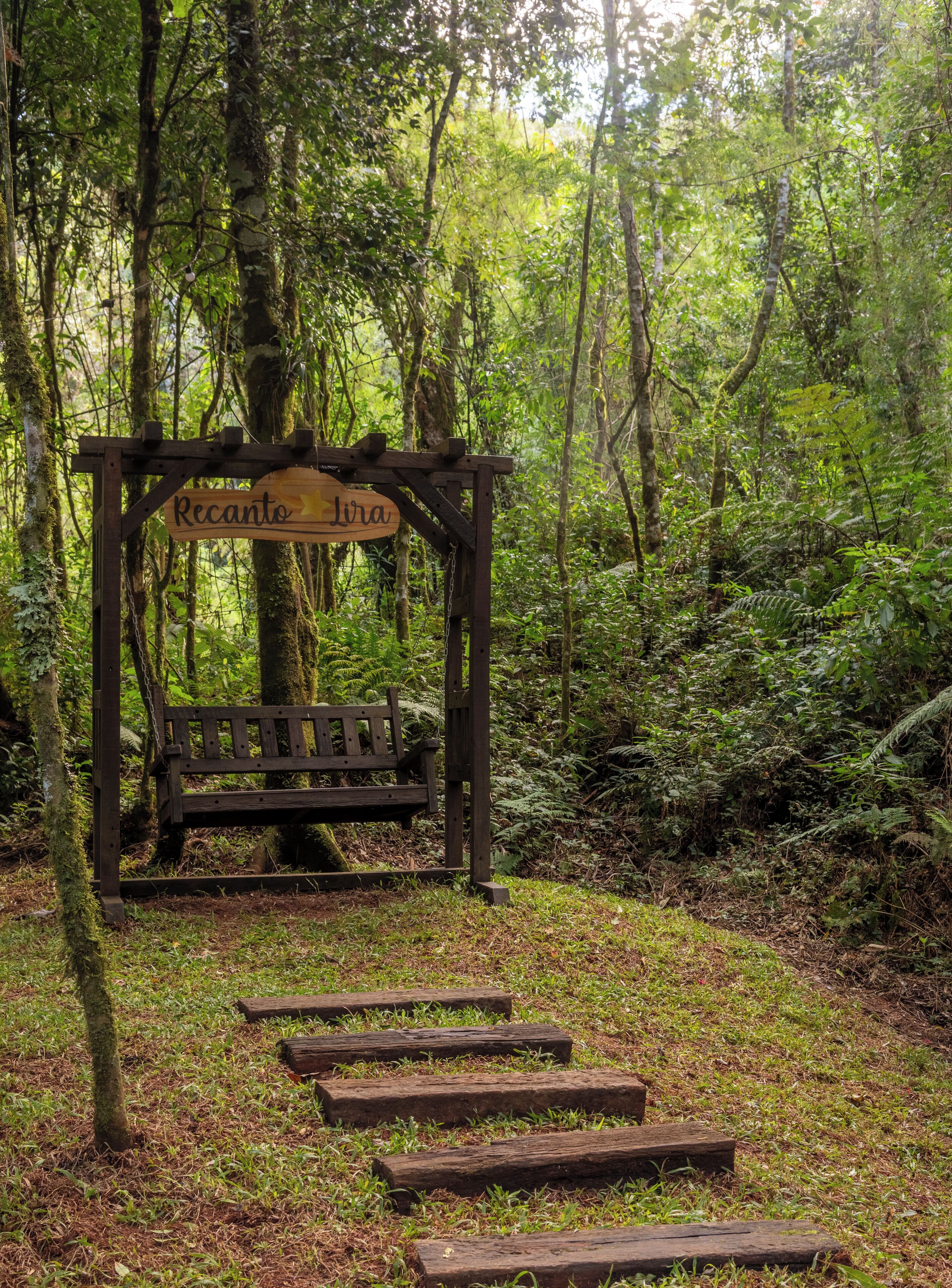 A wooden bench under a signpost in a forested area with steps leading up to it.