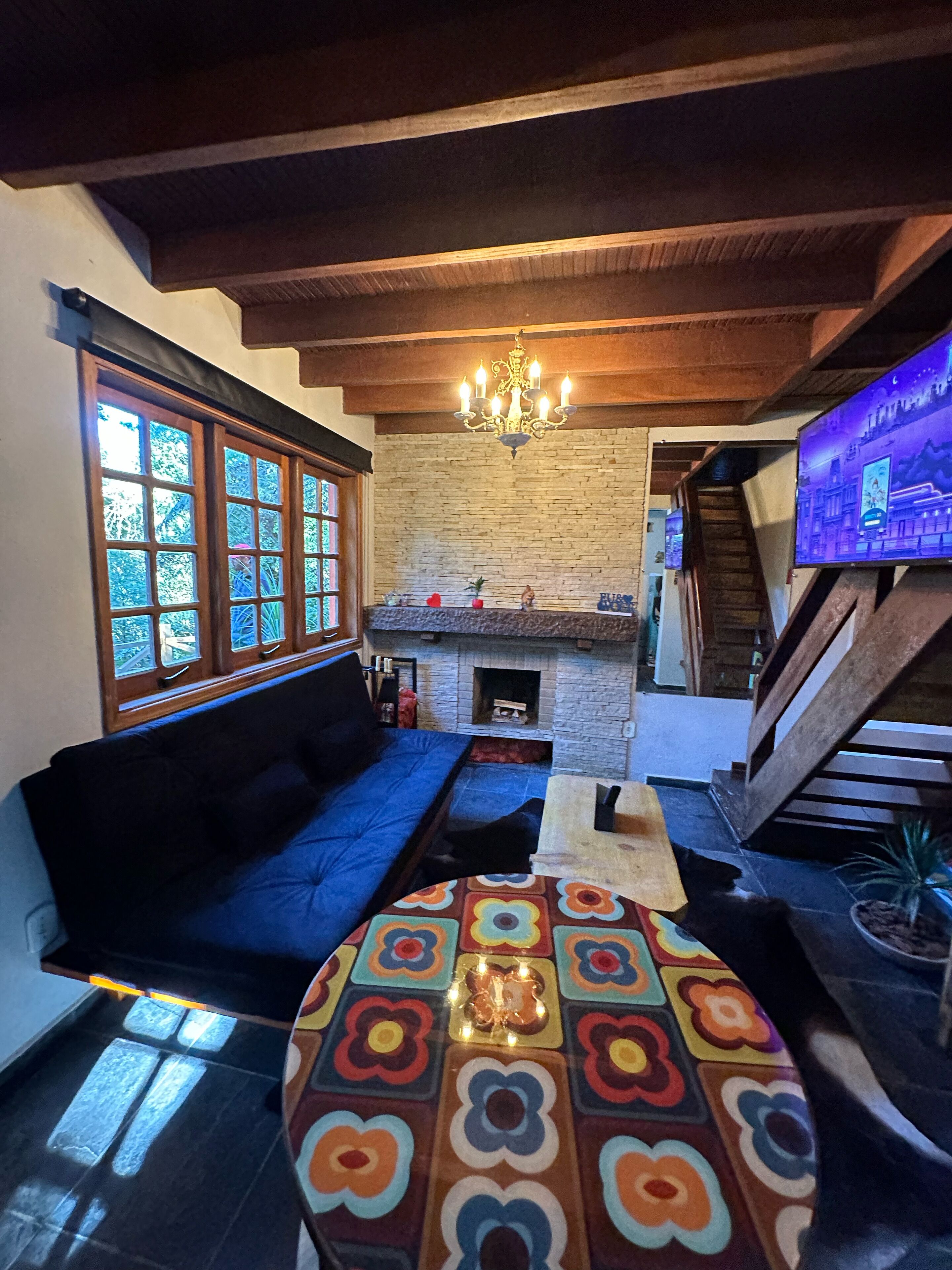 A cozy living room with a stone fireplace, a blue sofa, a colorful ottoman, and a chandelier.